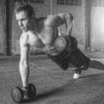 Male in press up position lifting dumb bells with a smooth waxed torso